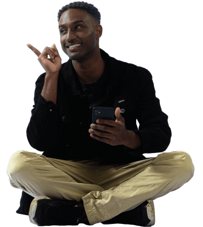 Menino negro sentado no chão com perna cruzada segurando o celular.